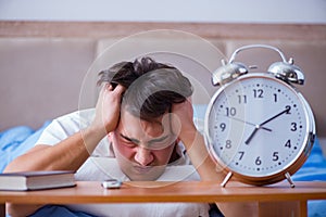 Man in bed frustrated suffering from insomnia with an alarm cloc