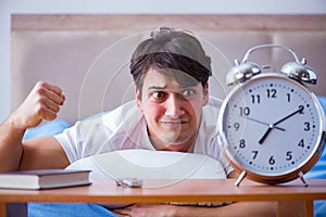 Man in bed frustrated suffering from insomnia with an alarm cloc