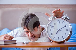 Man in bed frustrated suffering from insomnia with an alarm cloc