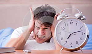Man in bed frustrated suffering from insomnia with an alarm cloc