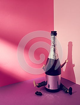 Man, behind a bottle of sparkling wine with arms and legs raised. Doll. Pink violet background. Text space. Party, celebration.