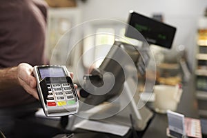 Man behind counter at a cafe offering credit card terminal