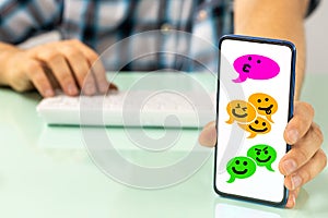 The man behind the desk shows the phone with comic speech bubbles of people talking via social messengers, Hand-drawn happy faces