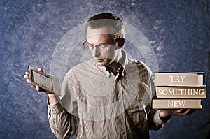 Man being focused on light and handy ebook reader, holding heavy books in other hand, try something new written on books.