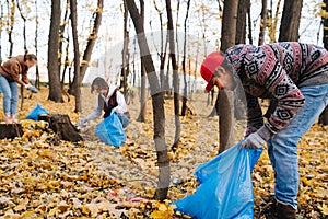 Man bending over, picking up trash in a seasonal forest at autumn