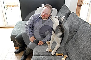 A man bent his ear to Husky& x27;s face on the sofa