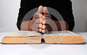 Man with a bible praying with hands clenched together