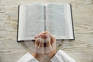Man with Bible praying at white wooden table, above view