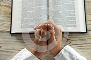 Man with Bible praying at white wooden table, above view