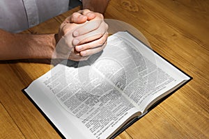 Man with Bible praying at wooden table, closeup