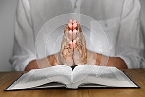 Man with Bible praying at wooden table, closeup