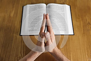 Man with Bible praying at wooden table, closeup