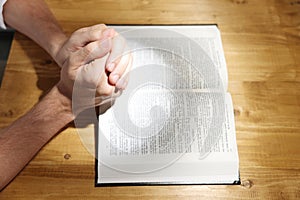 Man with Bible praying at wooden table, closeup