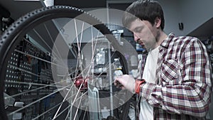 A man is a bicycle mechanic repairing a wheel in a bike store workshop. A bicycle mechanic fixes and adjusts the spoke