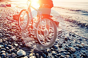 Man with bicycle on a sea shore sunset.