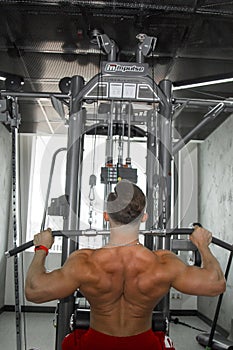 A man with big muscles is engaged in weightlifting in the gym. A pumped-up athlete goes in for sports on heavy weight simulators.