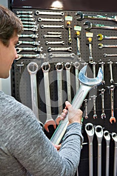 Man with big wrench near wall with tools in store