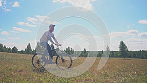 A Man Bike Traveler Rides His Bicycle On A Green Meadow On A Sunny Day. Healthy Man with Cycling Along Enjoying the