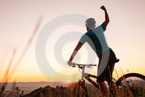 Man biker man meets a sunset in top of hill. He rising a one arm greeting on another successful day ending. Active sport people