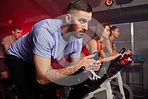 man biking in spinning class with friends at gym exercising on stationary bike