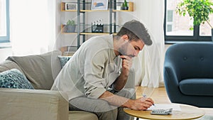 Man with bills counting on calculator at home