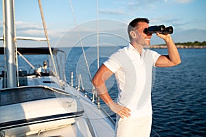 Man with binocular standing on a yacht deck