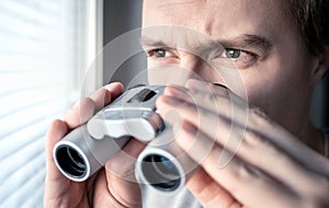 Man with binoculars. Private detective, agent or investigator looking out the window. Man spying or investigating.