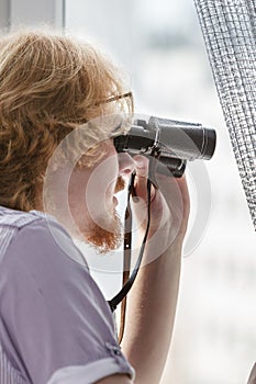 Man with binoculars spying on neighbors