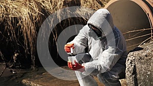 Man in bio-hazard suit and gas mask checks the pollution of the water outside