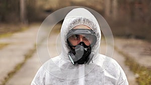 Man in bio-hazard suit and gas mask looks straight into the camera