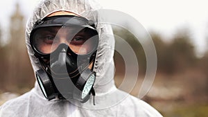 Man in bio-hazard suit and gas mask looks straight into the camera