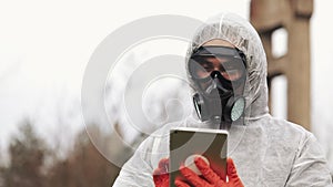 Man in bio-hazard suit and gas mask takes notes in his tablet standing on the polluted land