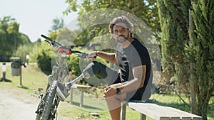 Man with bionic leg sitting on bench, holding handlebar of bike