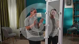 A man with bipolar disorder at a mirror in the living room. The man is writhing, laughing and mocking his reflection
