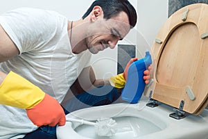 Man is a bit disgusted cleaning the toilet