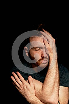 A man on a black background covers his face with his hands. The atmosphere of hopelessness,dejection photo