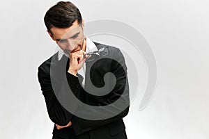 a man in a black business suit with a pensive look looks down glasses in his hands light background workflow. white