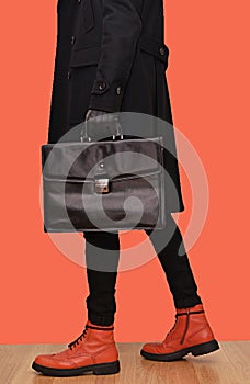 a man in a black coat with a black leather bag and orange boots