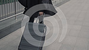 Man in black coat with black suitcase walking on background of airport terminal