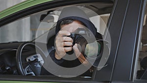 A private detective or photojournalist secretly takes photos from a car window with a long-focus lens.