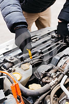 Man in black gloves checking the oil level in a car outdoors in winter. Car mechanic engineer working in car repair service. Male