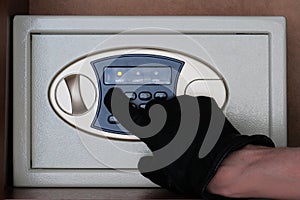 A man in black gloves enters a security code on the safe. The thief hacks electronic safe in the office or at home. Theft.