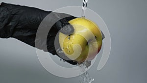 Man in black gloves hold green apple and wash it under water stream. Washing the green apple in hand with water splash