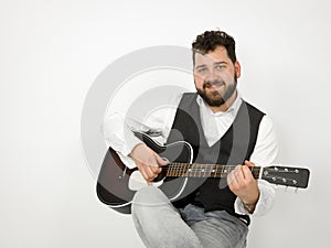 Man with black hair and beard playing and singing with acoustic guitar on white background and is happy