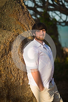 Man with black hair in a white shirt stands near the wall in the tropics at sunset