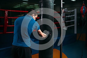Man in black handwraps exercises with bag in gym