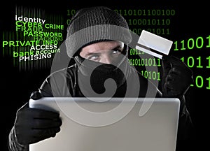 Man in black holding credit card using computer laptop for criminal activity hacking password and private information