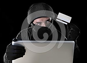 Man in black holding credit card using computer laptop for criminal activity hacking password and private information