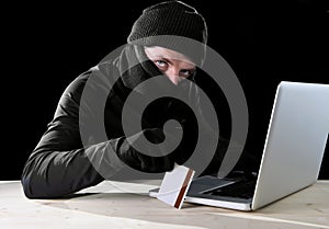 Man in black holding credit card using computer laptop for criminal activity hacking password and private information