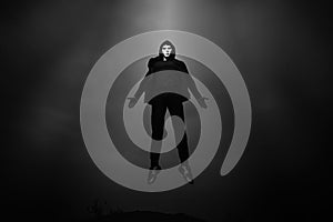 Man in black hoodie wearing white anonymous mask fly up in dark sky.